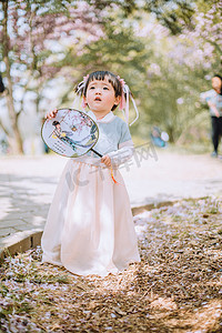 春游儿童白天可爱小女孩户外樱花树下拿着扇子抬头看摄影图配图