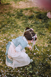 汉服小女孩白天小女孩户外蹲在地上捡花瓣摄影图配图
