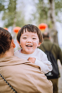 妈妈摄影照片_亲子春游白天被妈妈抱着的女儿公园大笑摄影图配图