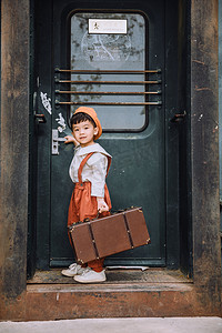 火车站人摄影照片_文艺复古儿童白天拎行李的小男孩户外火车站开火车门摄影图配图