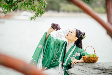 汉服美女白天汉服美女户外树下坐着喝酒摄影图配图