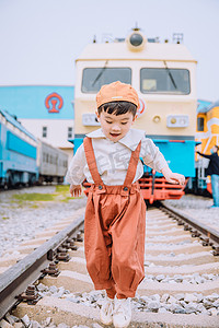 背带裤摄影照片_文艺复古儿童白天穿着背带裤的小男孩火车道走路玩耍摄影图配图