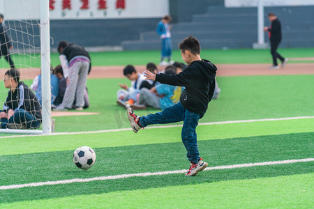 运动男孩摄影照片_儿童节白天男孩踢球操场运动摄影图配图