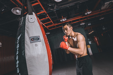 健身减脂增肌晚上运动的肌肉男生健身房打沙袋摄影图配图