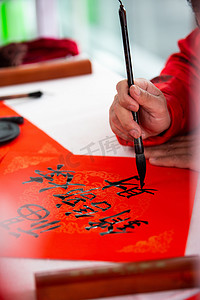 毛笔字春节摄影照片_过年白天写毛笔字的手室内写对联摄影图配图