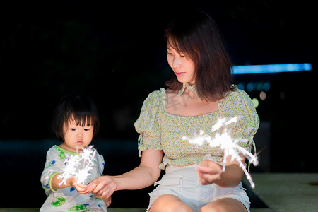 中秋国庆背景摄影照片_玩烟花的母女晚上母女户外正面摄影图配图