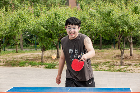 运动乒乓球摄影照片_运动白天打球的男生户外操场打乒乓球摄影图配图