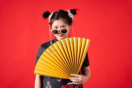 服装潮流摄影照片_国潮中国潮流女孩拿着折扇带着墨镜站着摄影图配图