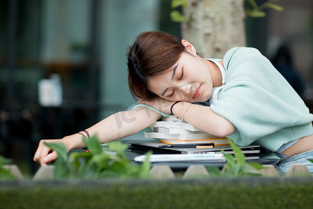 高考备战摄影照片_教育白天一个女学生户外趴在书本上睡觉摄影图配图