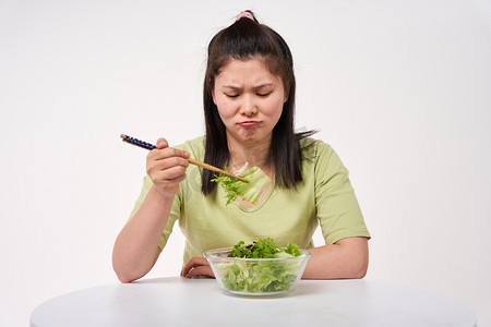 瘦身摄影照片_减肥肥胖女孩嫌弃地吃着沙拉摄影图配图