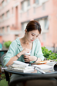 教育学习白天一个女学生户外一边看书一边打开咖啡摄影图配图