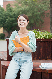 教育学习白天一个女学生户外抱着书坐着摄影图配图