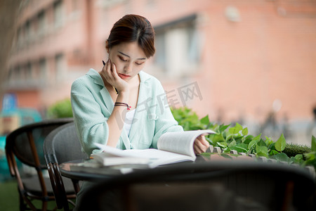 教育学习白天一个女学生户外托下巴看书摄影图配图