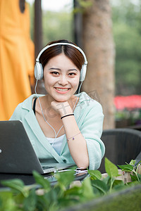 戴耳机的女生摄影照片_户外白天戴着耳机上网课的女生户外户外摄影图配图