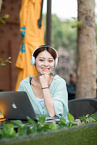 教育学习白天戴着耳机的女学生户外托下巴微笑摄影图配图