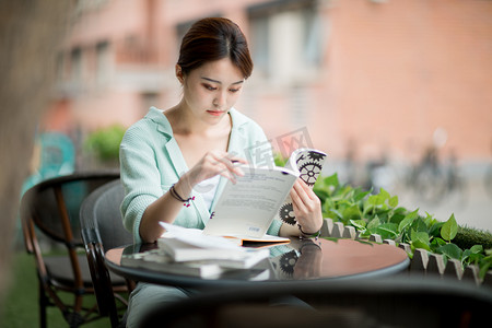 摄影照片_教育学习白天一个拿着书的女学生户外看书摄影图配图