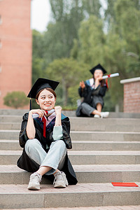毕业季白天穿着学士服的美女毕业生户外蹲在台阶上摄影图配图