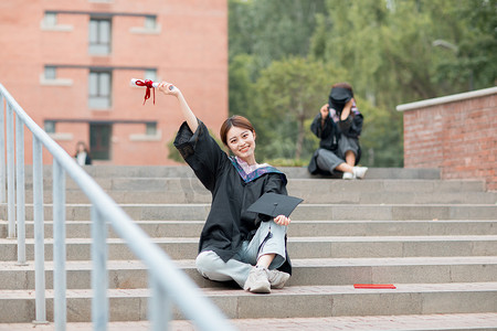 教育白天穿着学士服的美女毕业生教学楼外坐在台阶摄影图配图