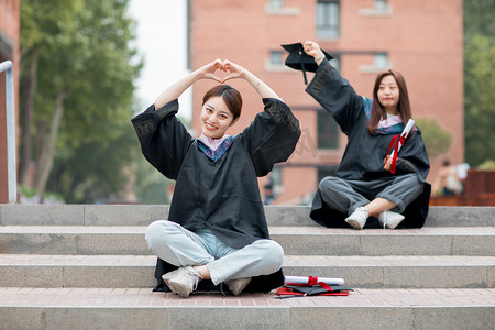 毕业季白天穿着学士服的美女毕业生户外比心摄影图配图