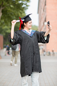 毕业摄影照片_毕业季白天穿着学士服的美女教学楼外自拍摄影图配图