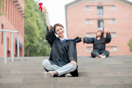 毕业季白天穿着学士服的两个美女毕业生户外举起毕业证摄影图配图