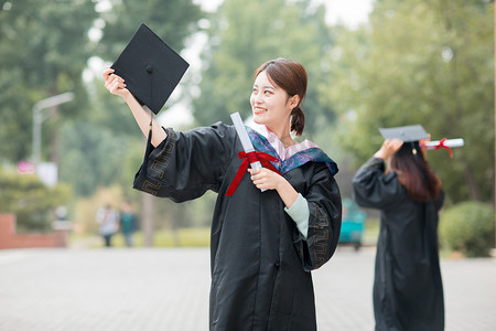 毕业季白天穿着学士服的美女毕业生户外举起学士帽摄影图配图