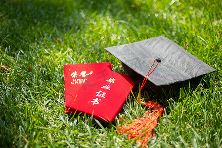 毕业季暑期毕业证和学士帽草地上展示摄影图配图