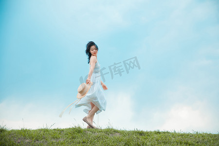 户外运动老外摄影照片_文艺清新白天穿着白裙的美女户外草坪跑步摄影图配图