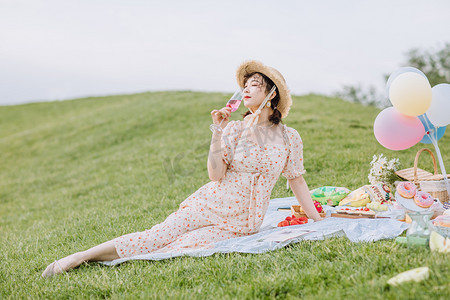 夏天文艺白天穿着碎花裙的美女户外草地喝酒摄影图配图