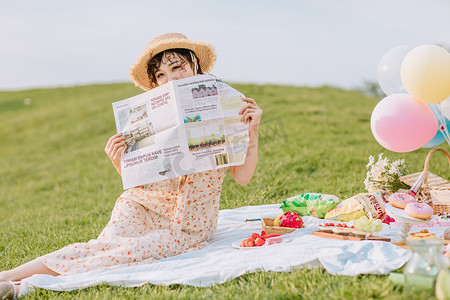 户外野餐摄影照片_文艺夏天白天野餐的美女户外拿报纸摄影图配图