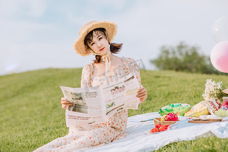 田野春天摄影照片_文艺夏天白天野餐的美女户外草地看报纸摄影图配图