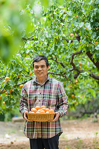 果农摄影照片_人物白天一个人果园端着果篮摄影图配图