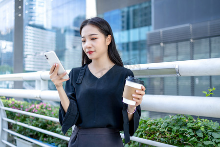 商务人像下午商务女性人行桥写字楼拿咖啡玩手机摄影图配图