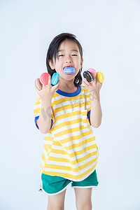 夏日儿童白天站着的男孩室内白背景双手拿马卡龙吃摄影图配图