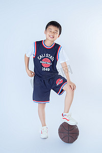 孩子篮球摄影照片_夏日运动人像白天帅气男孩室内白背景脚踩篮球摄影图配图