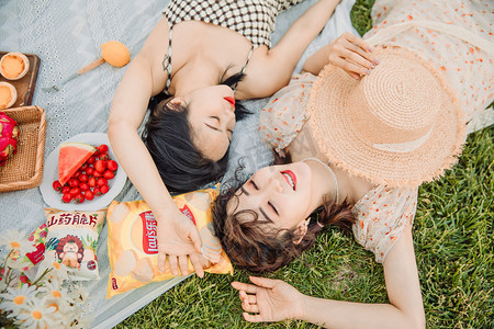 春游郊游摄影照片_野餐郊游白天两位美女户外草地躺在草地上摄影图配图
