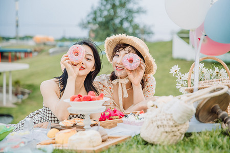 野餐郊游白天吃甜甜圈的闺蜜户外草地趴在草地上摄影图配图
