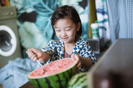 儿童夏日人像白天一个长发小男生室内高兴的吃西瓜摄影图配图