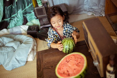 六一儿童节标题框摄影照片_夏日儿童白天小男孩室内坐桌前拿西瓜摄影图配图