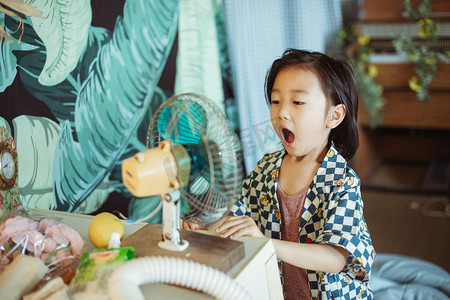 人像小孩摄影照片_夏日儿童人像白天帅气小男孩室内张嘴吹风扇摄影图配图