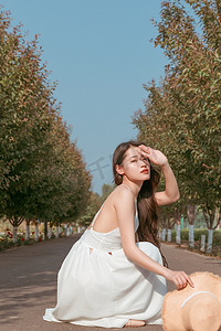 春游的摄影照片_夏天文艺美女白天穿着白色长裙的美女户外公园蹲着摄影图配图