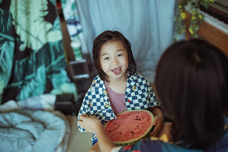 快乐的儿童节摄影照片_夏日亲子白天母子室内抱着西瓜吐舌头摄影图配图