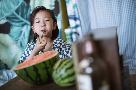 夏日儿童白天长发小男孩室内用勺吃西瓜摄影图配图