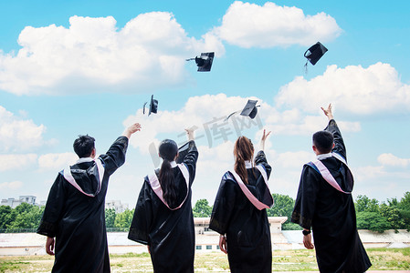 学士帽学士摄影照片_人像白天四个大学生操场扔学士帽摄影图配图