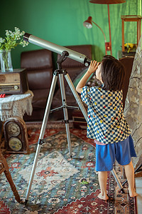 帅气的小男孩摄影照片_夏日儿童白天小男孩室内看望远镜摄影图配图
