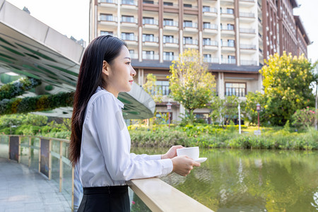 商务下午白领女性湖边拿着咖啡侧脸摄影图配图