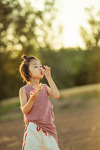 畅享夏日瓜分幸福摄影照片_夏日儿童人像夕阳长发小男孩田地旁吃手吃西瓜摄影图配图