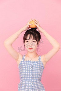 少女粉面摄影照片_夏季白天元气美女室内水果橙子摄影图配图