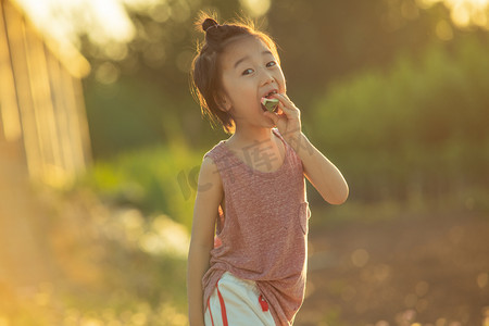 西瓜男孩摄影照片_夏日儿童人像夕阳长发男童麦田开心吃西瓜摄影图配图