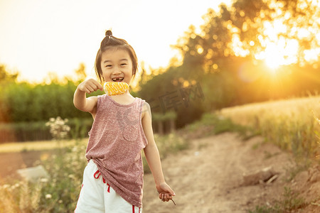 小孩开心笑摄影照片_夏日儿童人像夕阳长发小男孩麦田开心拿着冰棍摄影图配图